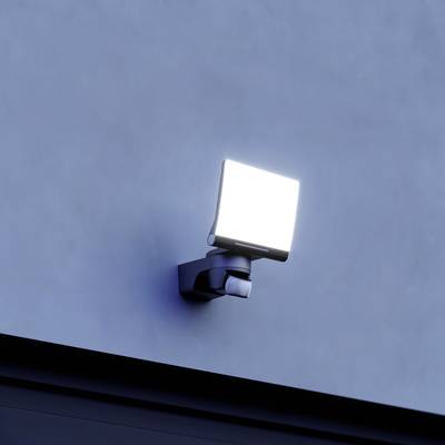 Eine leuchtende Außenlampe an einer Wand in der Dämmerung, die die Umgebung mit hellem Licht erhellt.