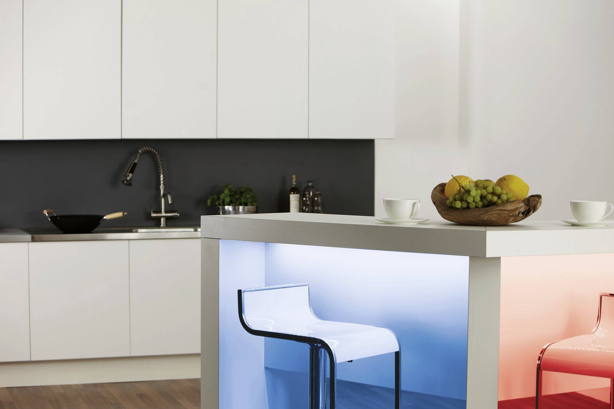 Ein moderner Küchenbereich mit weißem Schrank, schwarzer Arbeitsplatte, Wasserhahn und beleuchtetem Küchentresen. Ein Fruchtkorb steht auf der Theke.