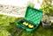 Eine grüne, offene Box mit mehreren gelben Steckdosen und Kabeln steht auf dem Gras. Daneben sind Pflanztöpfe und ein Kiesweg zu sehen.
