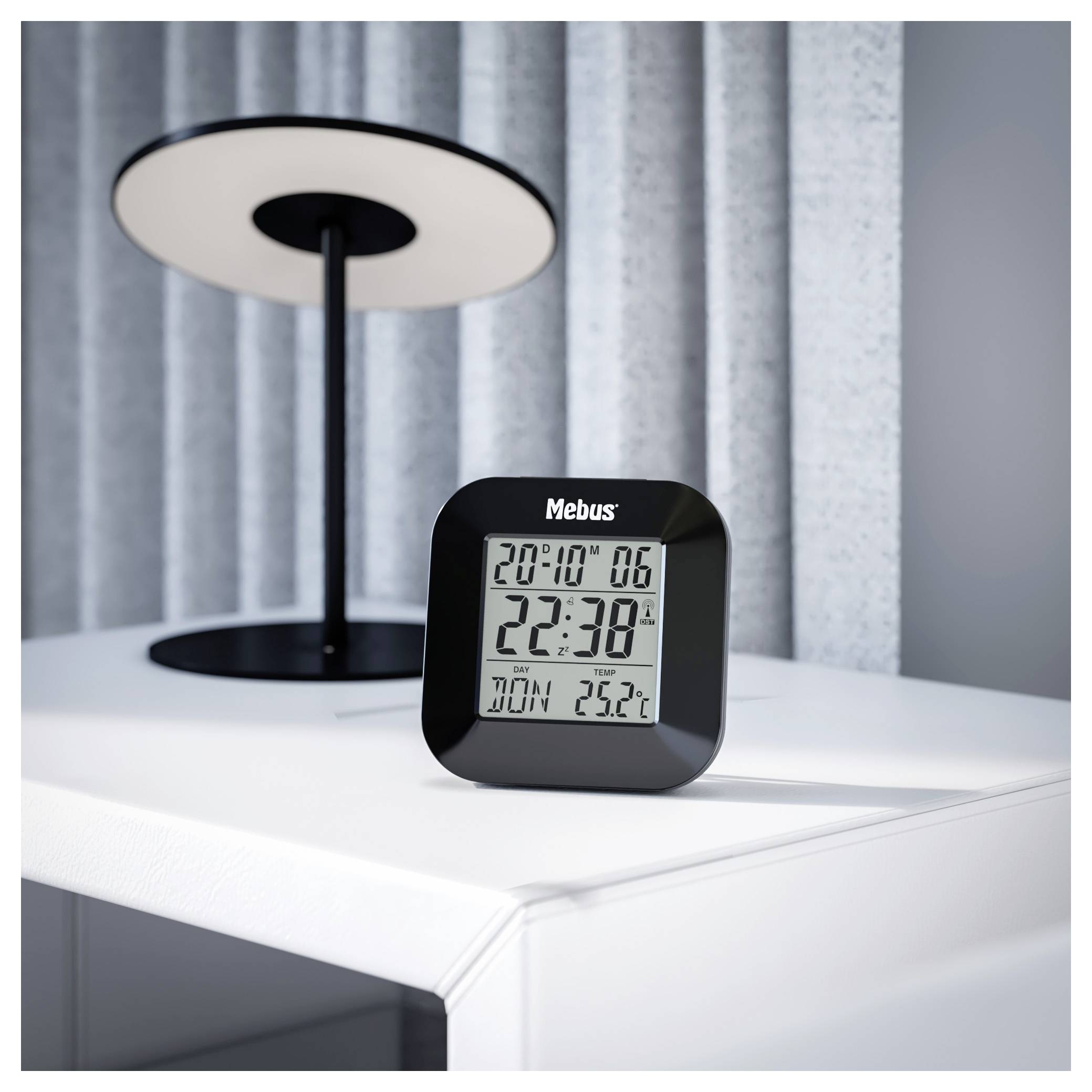 Eine Digitaluhr zeigt "20:10" und "22:38" an, daneben steht "So 25°C" neben einer Lampe auf einem weißen Tisch.