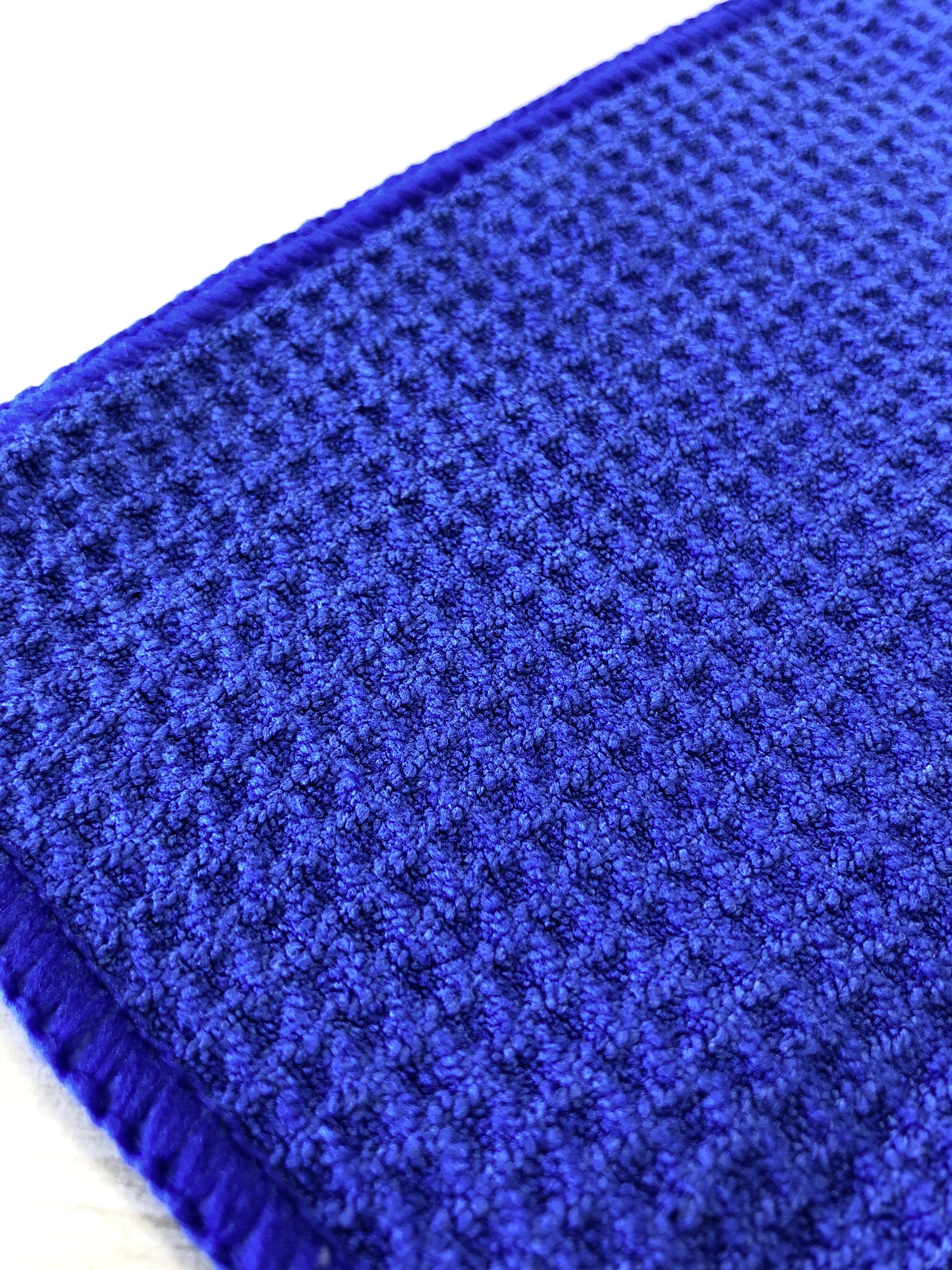Ein blauer Stoff mit Waffelmuster-Textur. Der Stoff hat eine rechteckige Form und liegt auf einer weißen Oberfläche.