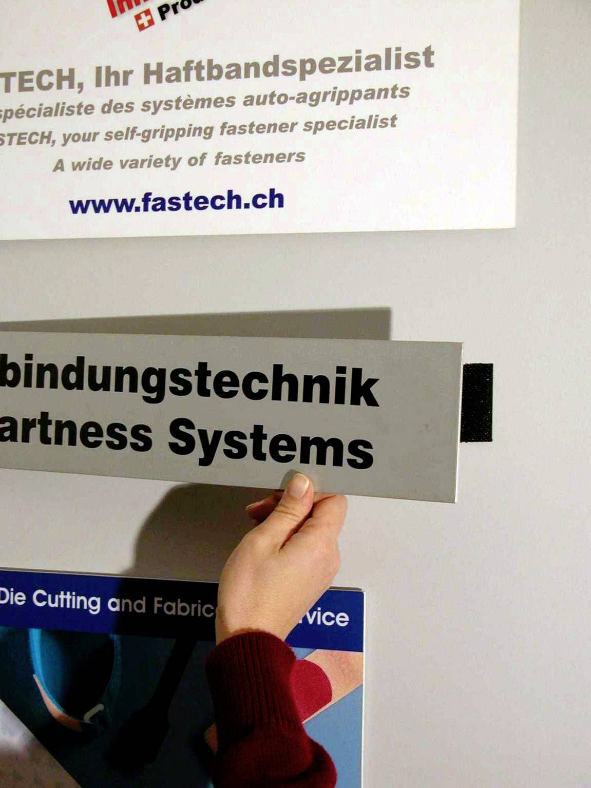Person hält ein Schild mit der Aufschrift 'Verbindungstechnik Partner Systems'. Im Hintergrund sind Informationsschilder sichtbar.