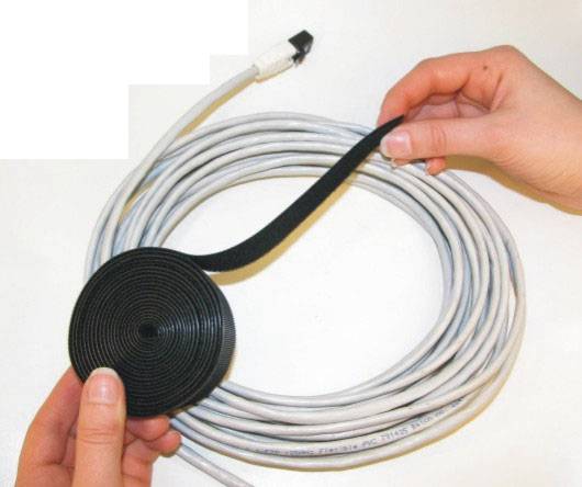 Hände wickeln ein weißes Kabel mit einem schwarzen Klettband zu einer Rolle zusammen.