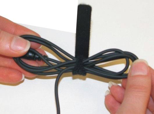 Eine Hand hält ein zusammengebundenes Kabel, das mit einem Klettband fixiert ist, auf weißem Hintergrund.