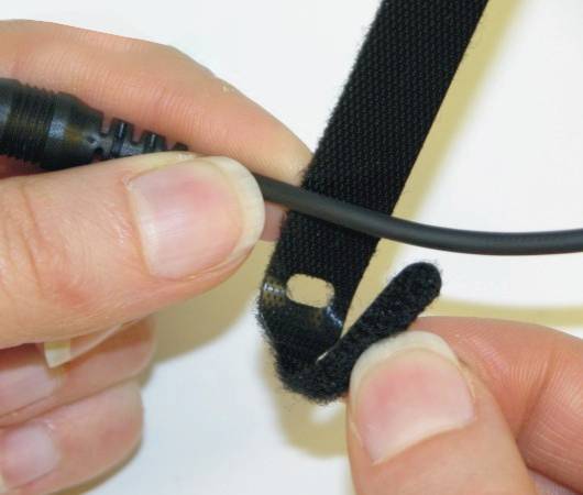 Nahaufnahme von Händen, die ein schwarzes Kabel mit einem Klettband sichern.