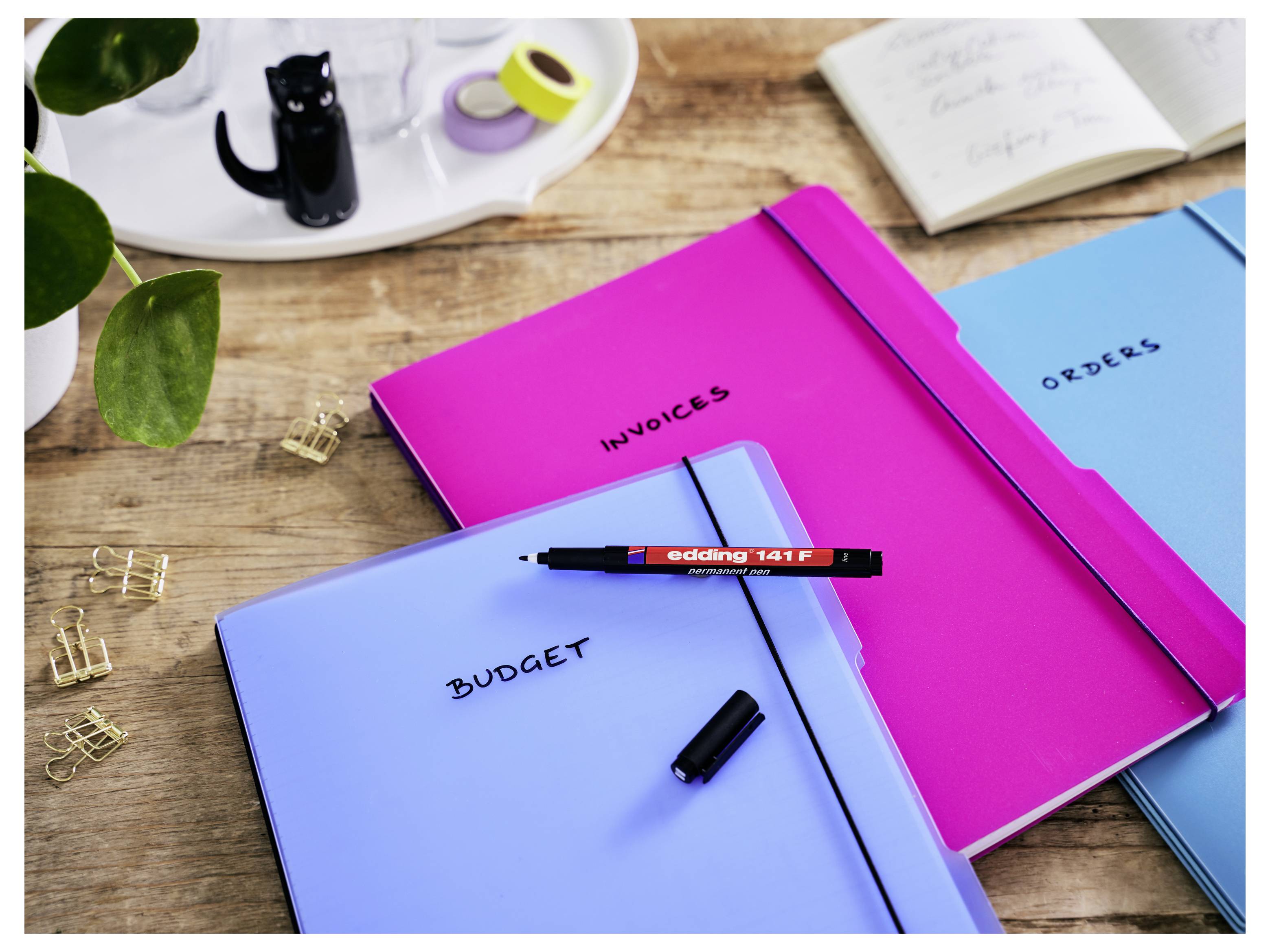 Schreibtisch mit beschrifteten Ordnern „BUDGET", „INVOICES" und „ORDERS", sowie Stift und Büromaterial, was auf die Organisation von Geschäftsdokumenten hindeutet.