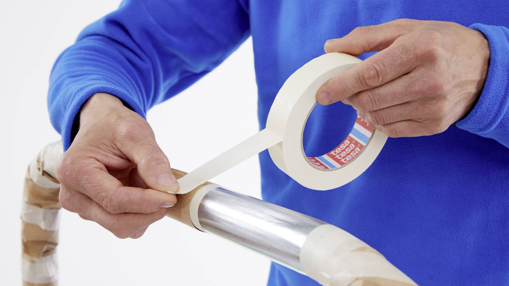 Eine Person wickelt Klebeband um ein Metallrohr, möglicherweise für eine Bastel- oder Reparaturarbeit.