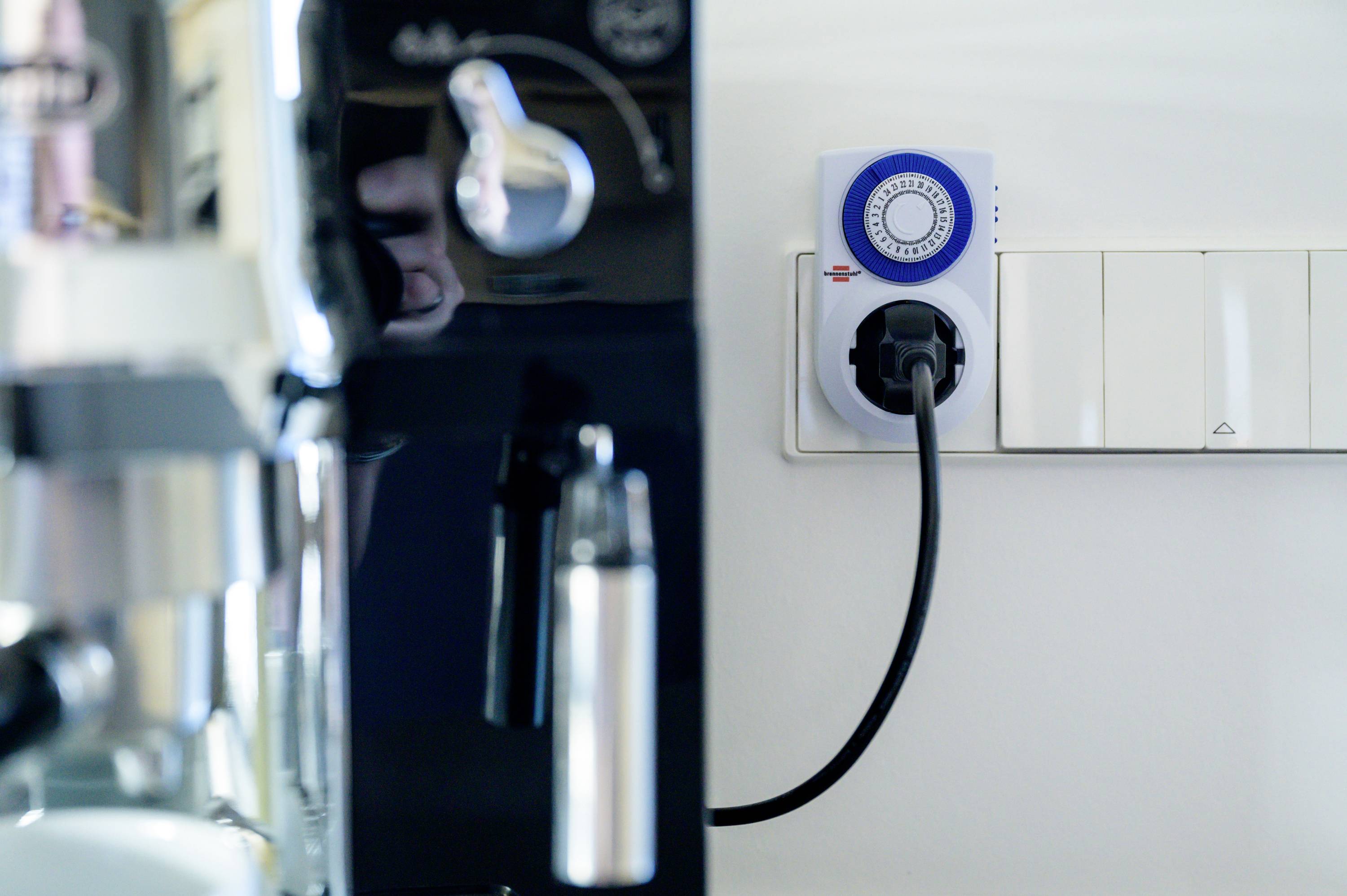 'Nahaufnahme einer Kaffeemaschine angeschlossen an eine Steckdose mit mechanischem Timer. Der Timer ist auf eine bestimmte Zeit eingestellt.'
