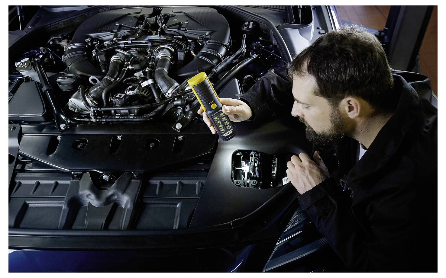 Ein Mechaniker inspiziert einen Automotor mit einem tragbaren Diagnosegerät unter der offenen Motorhaube.