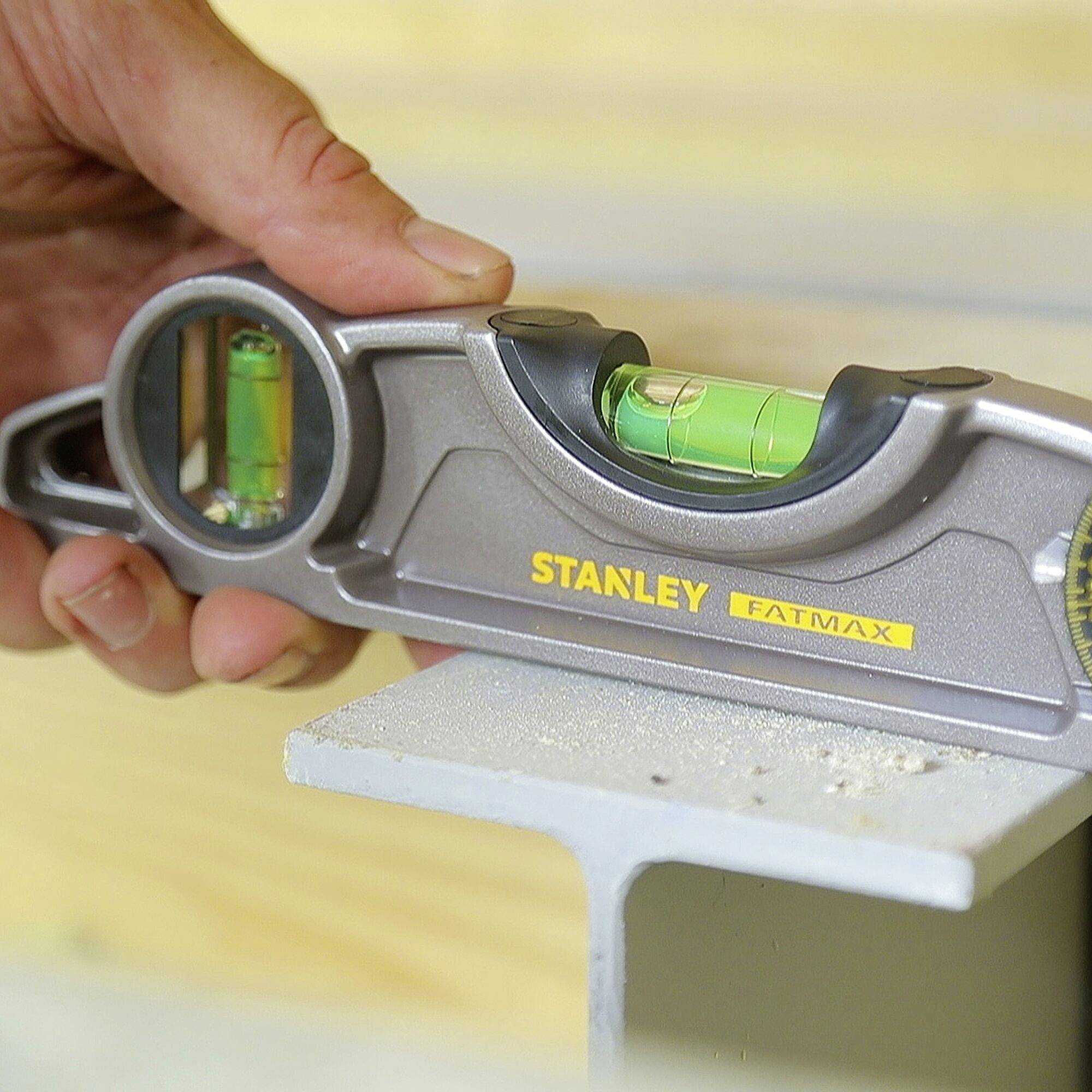 Eine Hand hält eine Stanley Wasserwaage über einer Metalloberfläche, um deren Ebenheit zu überprüfen.