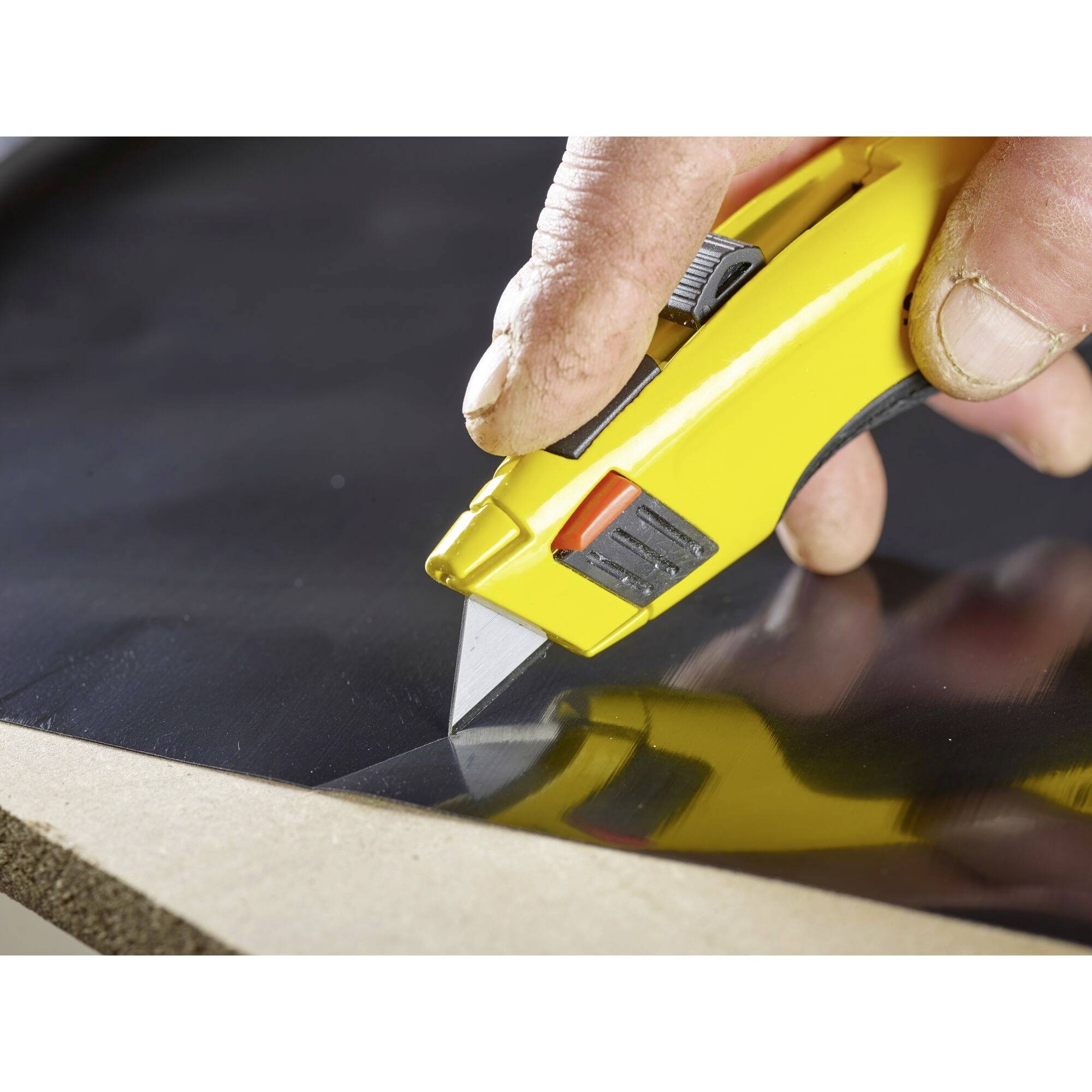 Hand schneidet mit gelbem Cutter-Messer Material auf Holzplatte.