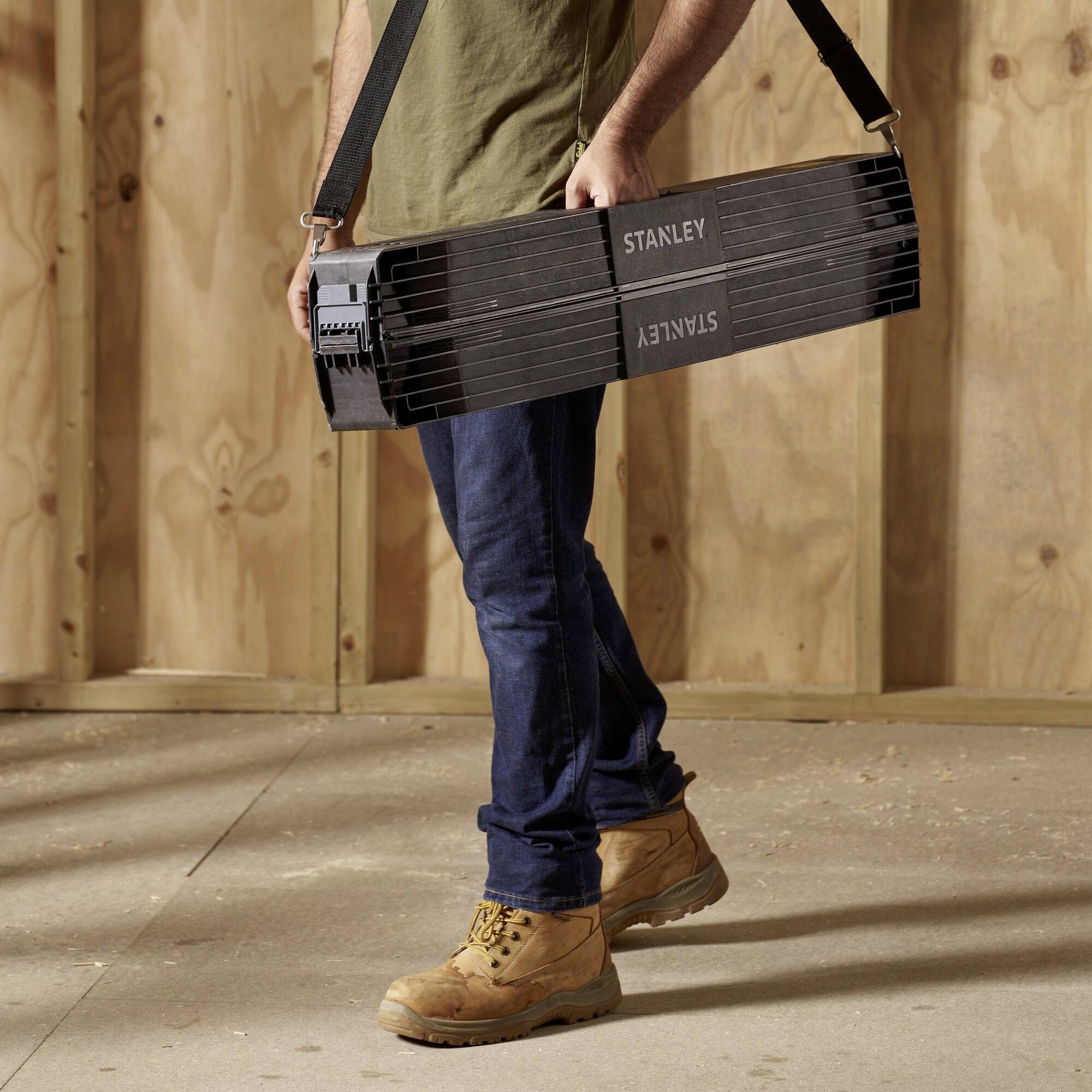 Person trägt einen schwarzen Stanley-Maßstab in einem Holzrahmenbau.