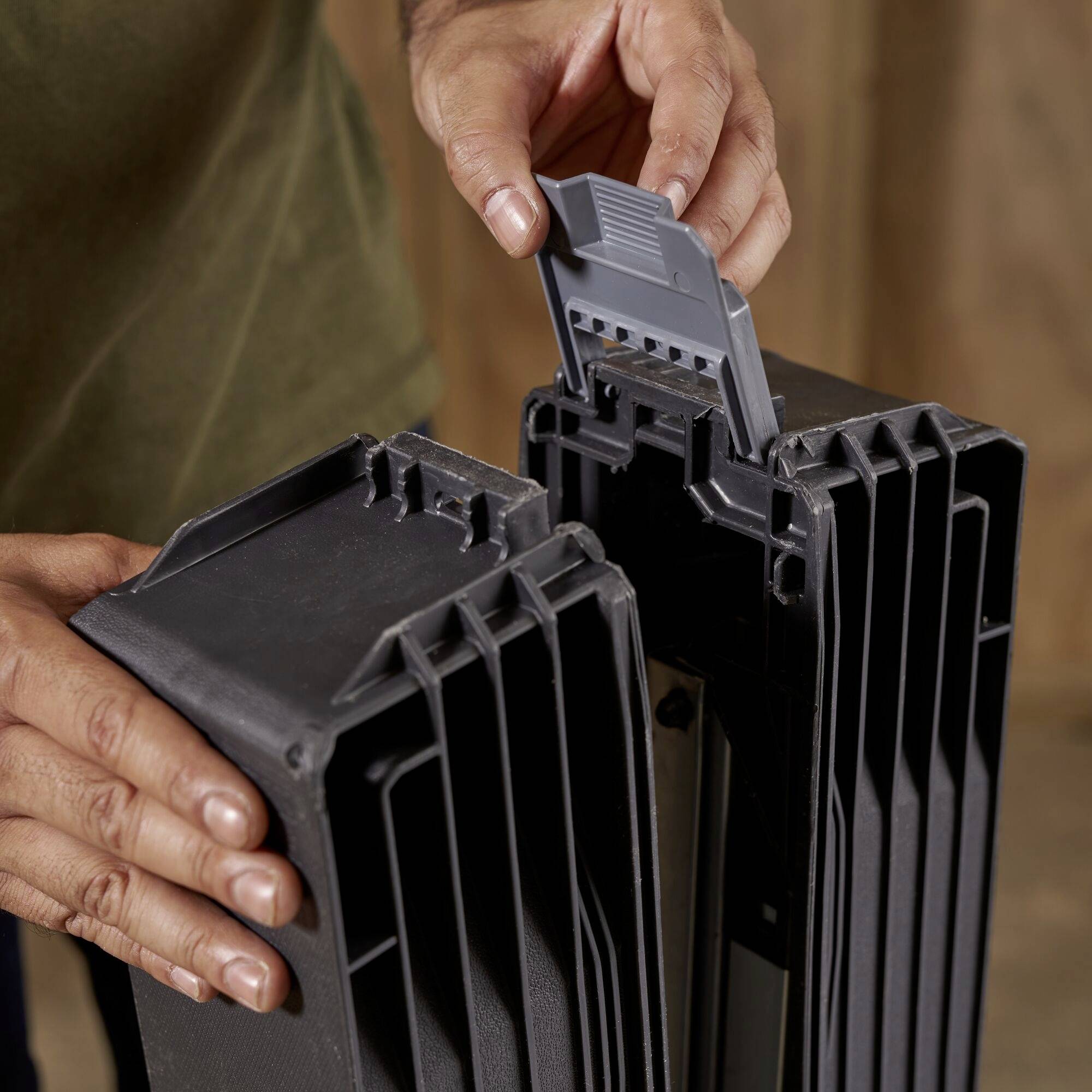 Eine Person steckt einen Kunststoffkamm in die Rückseite eines schwarzen Kunststoffelements.