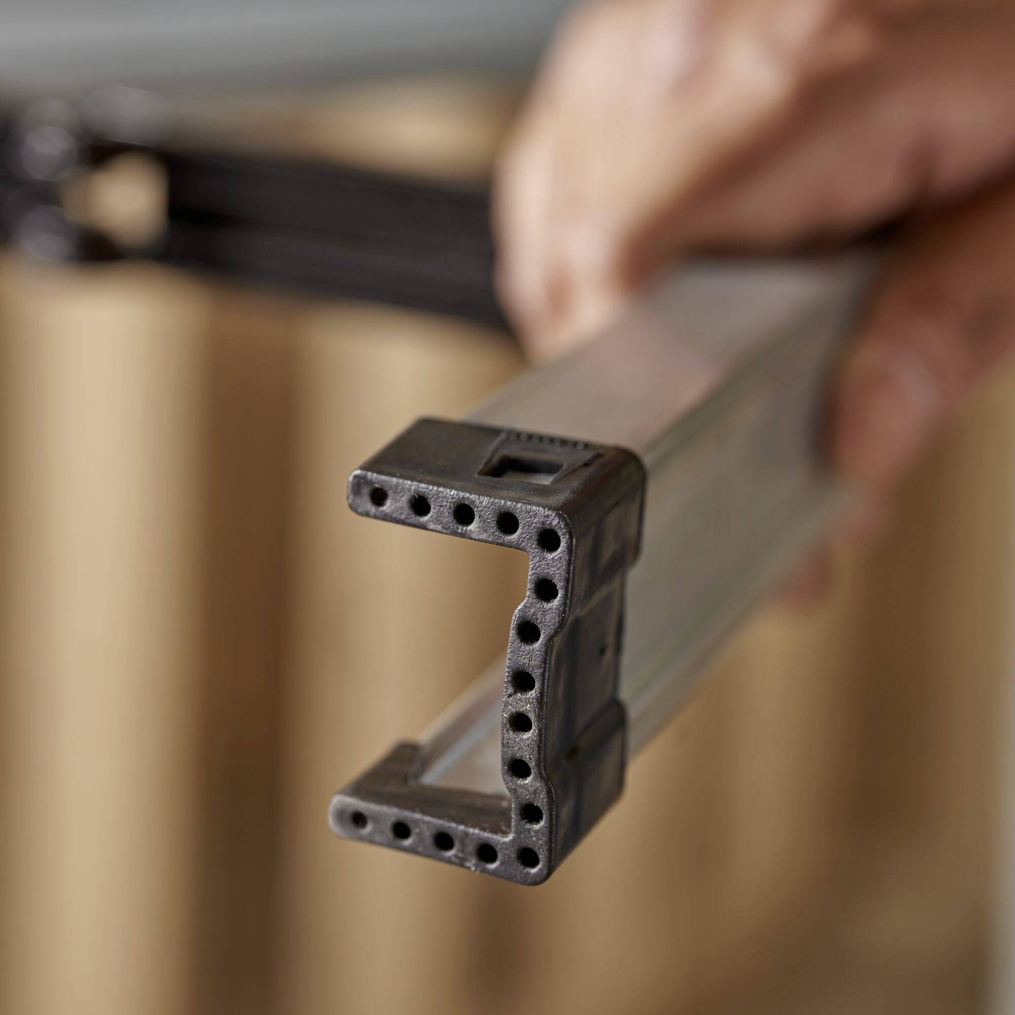 Nahaufnahme eines rechteckigen Metallprofils mit gebohrten Löchern in der Vorderansicht, von einer Hand gehalten.