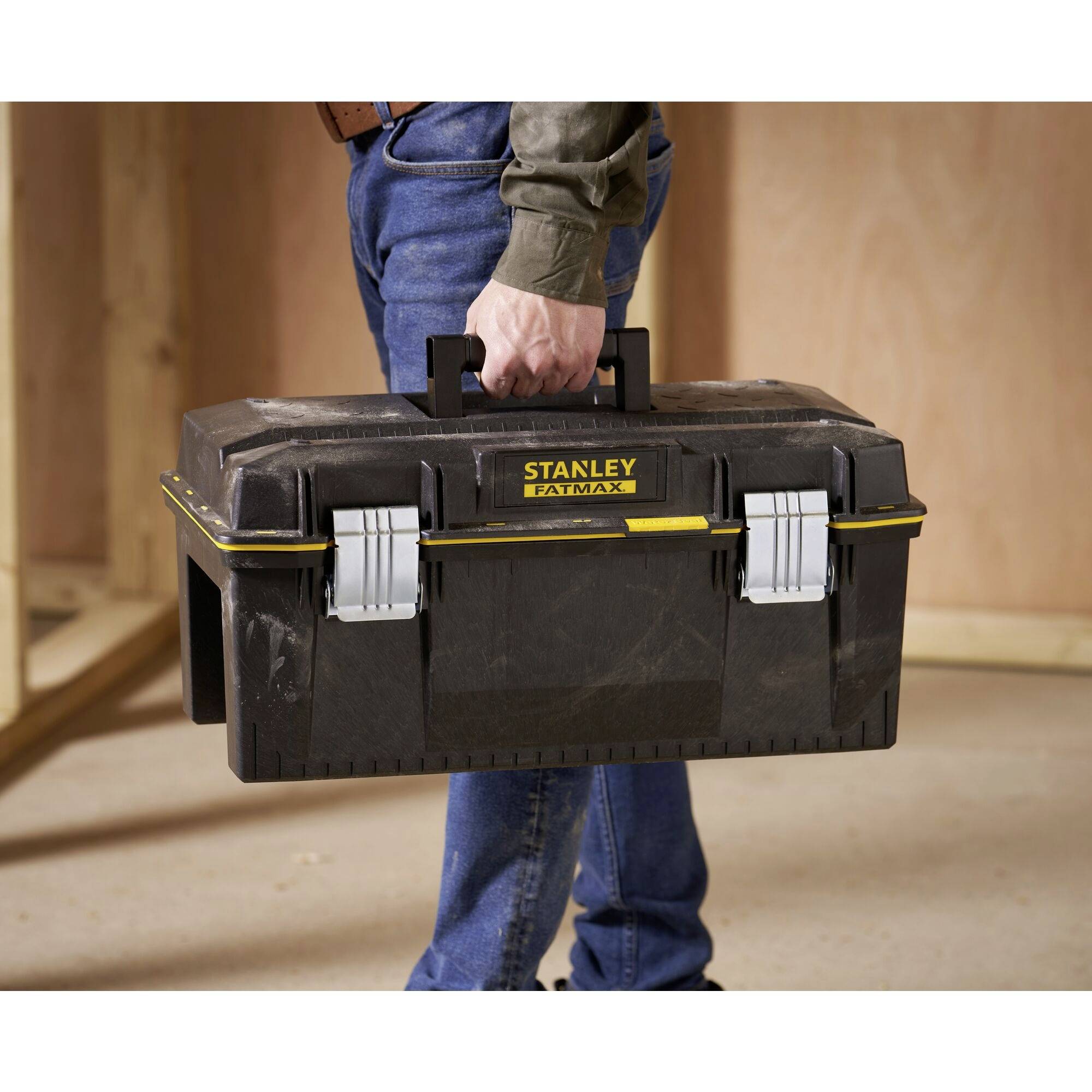 Eine Person hält einen schwarzen Werkzeugkasten von Stanley Fatmax in der Hand. Der Kasten ist geschlossen und befindet sich in einer Werkstattumgebung.