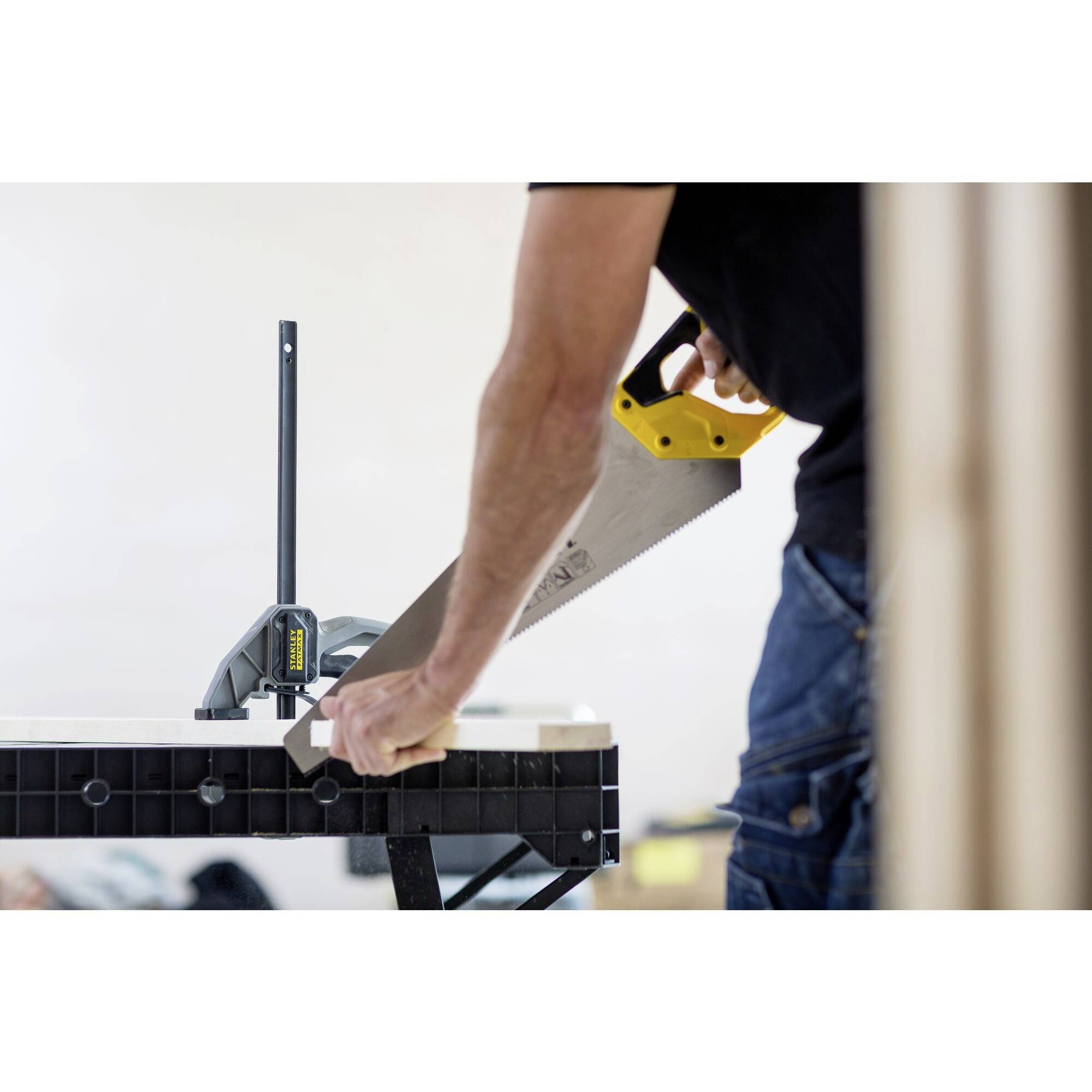 Eine Person sägt mit einer Handsäge ein Stück Holz, das in einer Werkbank eingespannt ist. Es scheint eine handwerkliche Tätigkeit zu sein.