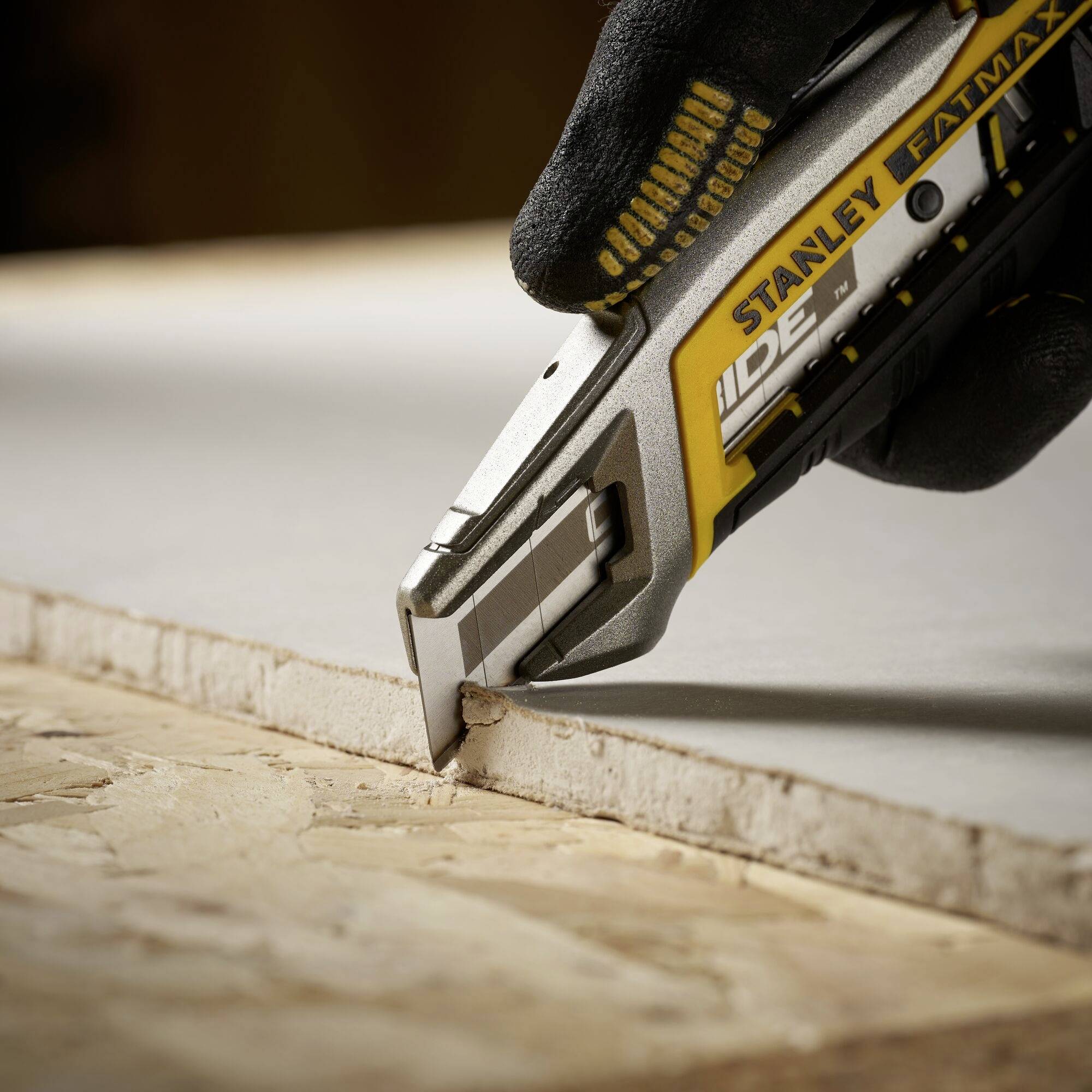 Eine Person schneidet mit einem gelben Stanley Fatmax Teppichmesser präzise eine dünne Platte. Hand in schwarzem Handschuh.