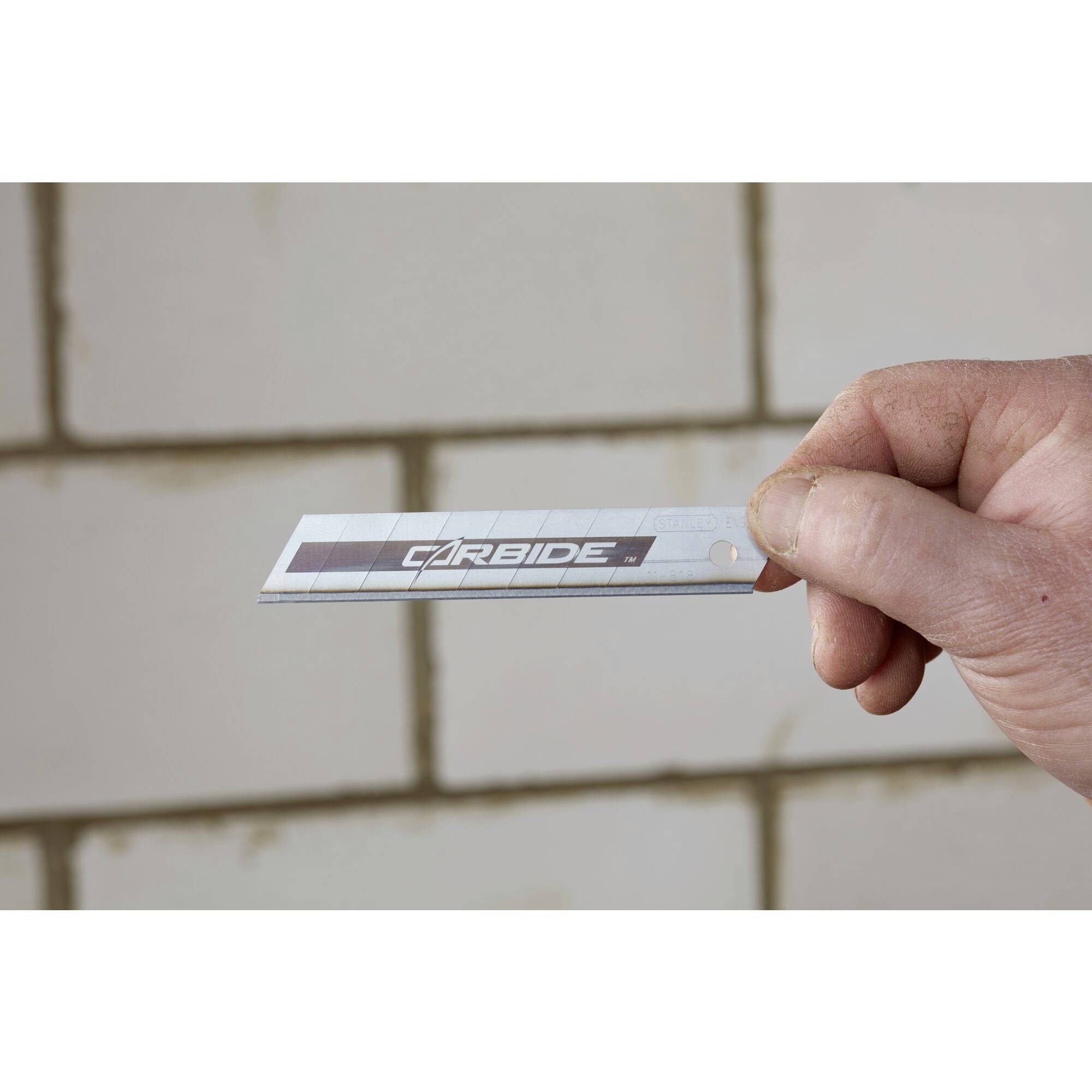 Eine Hand hält ein Klingenmesser mit der Aufschrift 'CARBIDE', vor einem gefliesten Hintergrund.