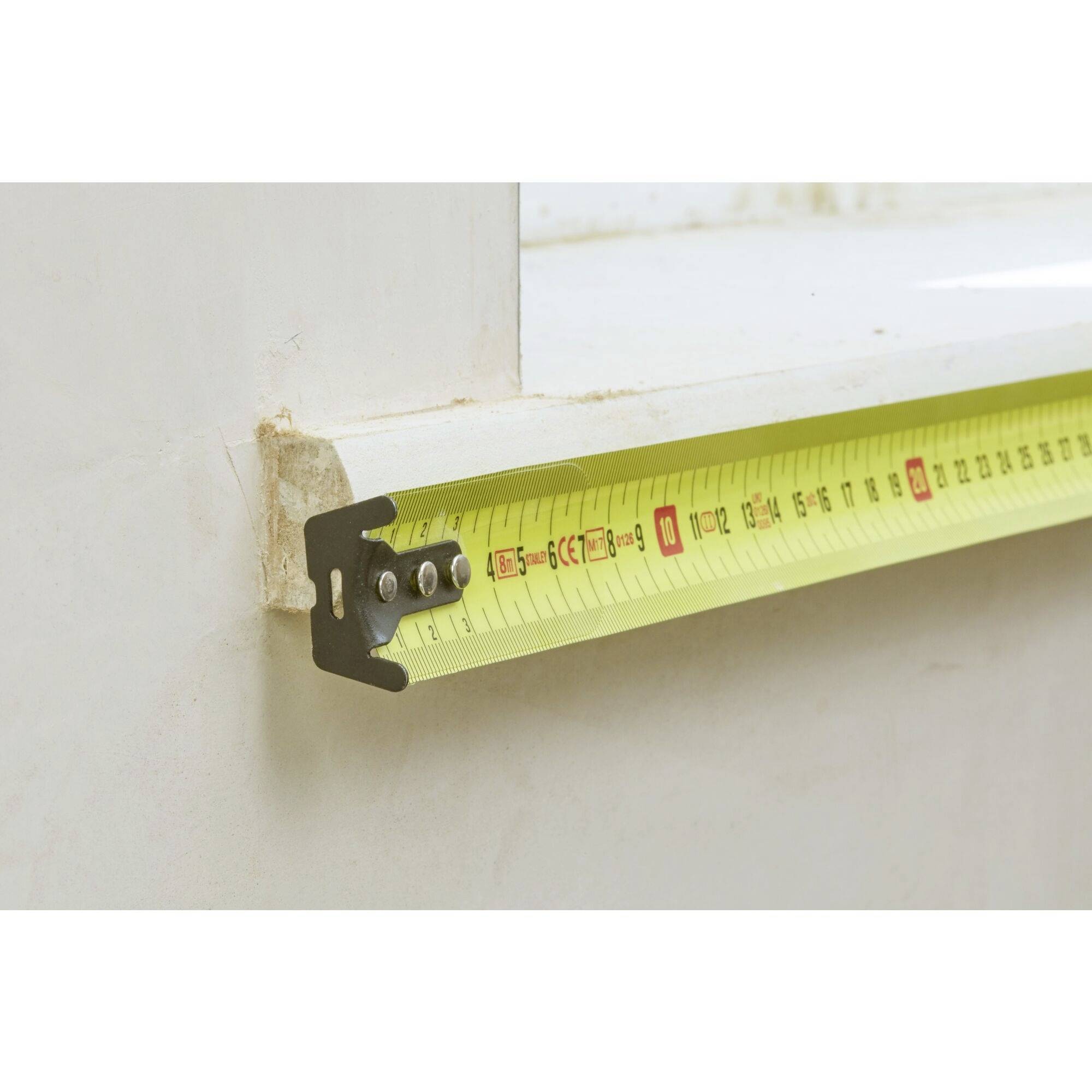 Ein gelbes Maßband zeigt eine Länge von etwa 15 cm an, das an einem Fensterrahmen entlanggemessen wird.