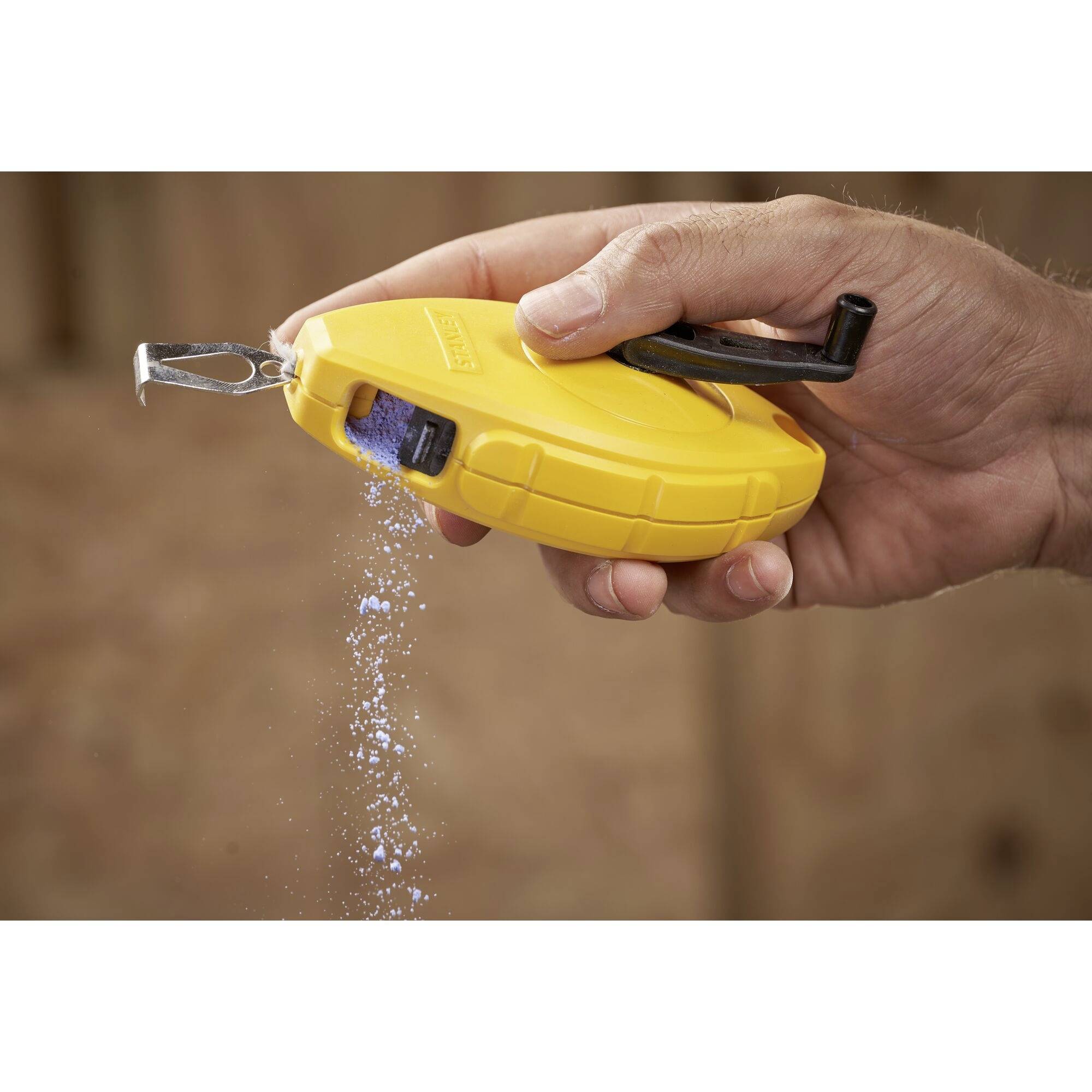 Eine Hand hält ein gelbes Kreide-Schnurgerät, aus dem blaue Kreide auf eine Holzoberfläche rieselt.