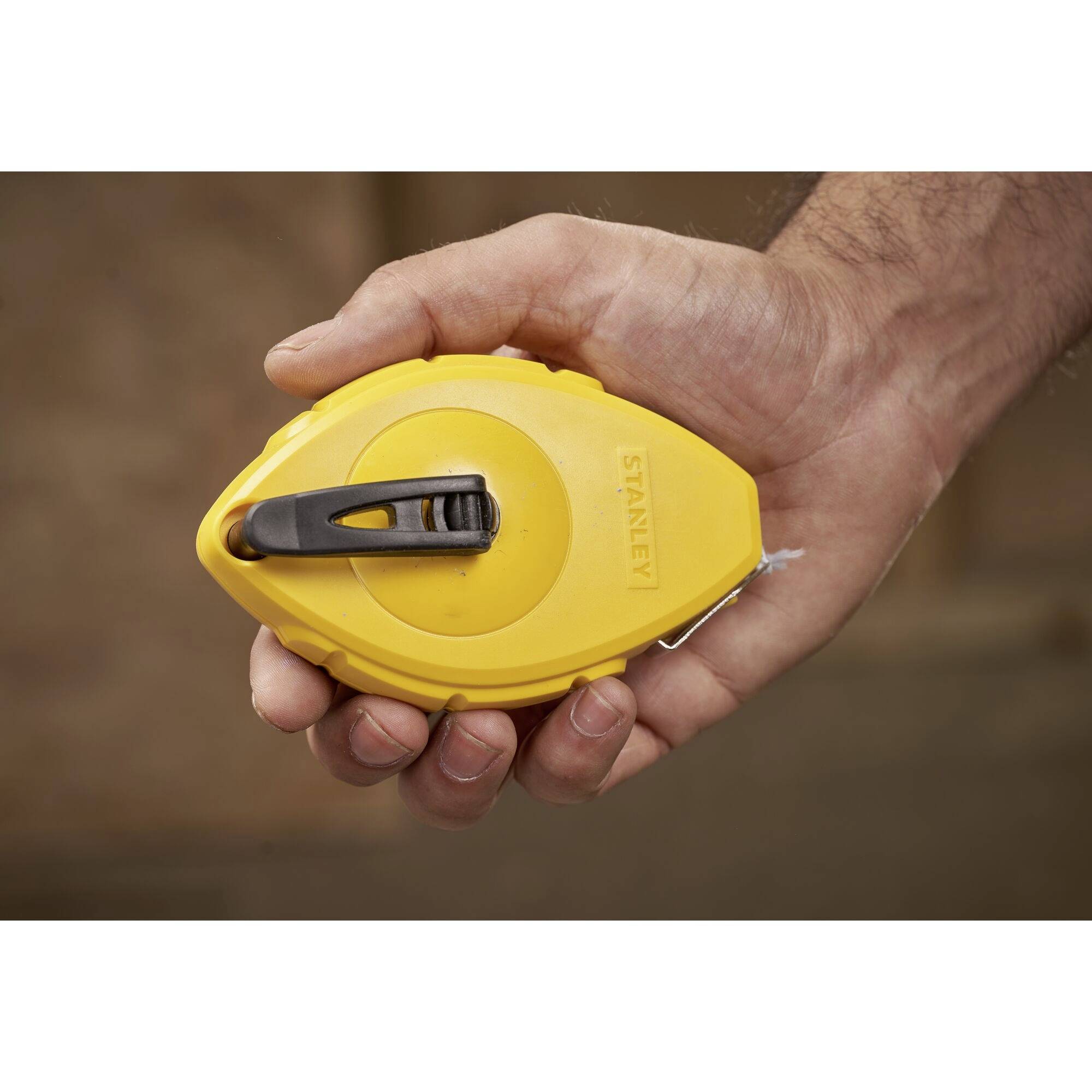 'Männliche Hand hält ein gelbes Maßband mit schwarzem Clip.'