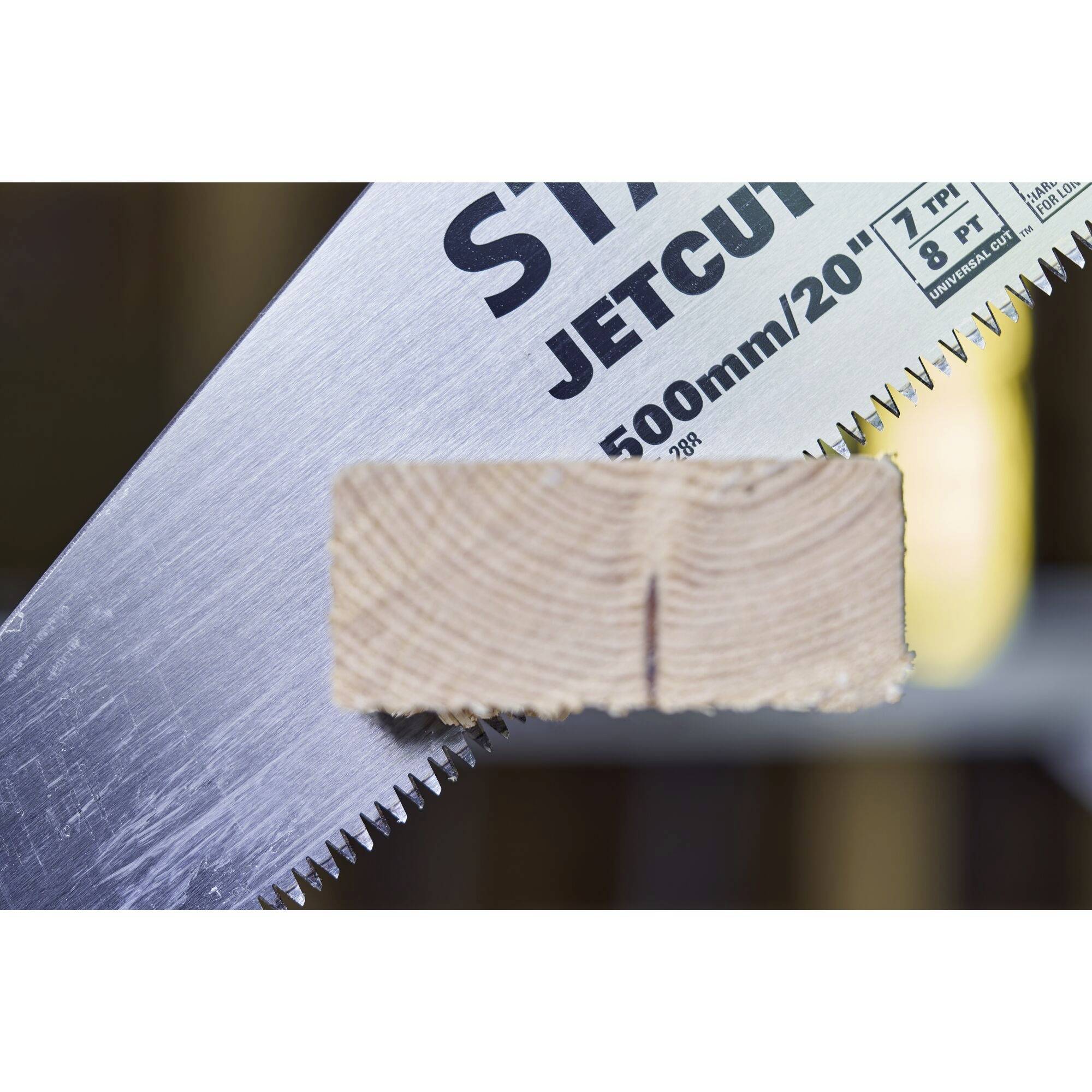 Nahaufnahme einer Säge mit der Aufschrift 'JETCUT 500mm/20"'. Ein Holzstück ist zwischen den Zähnen eingespannt, umgeben von unscharfem Hintergrund.