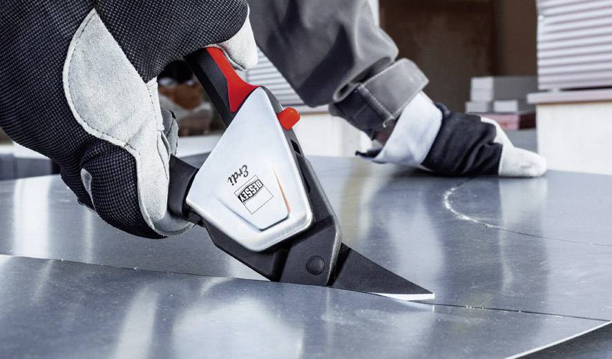 Eine Person trägt Arbeitshandschuhe und schneidet präzise ein Metallblech mit einem spezialisierten Schneidewerkzeug.