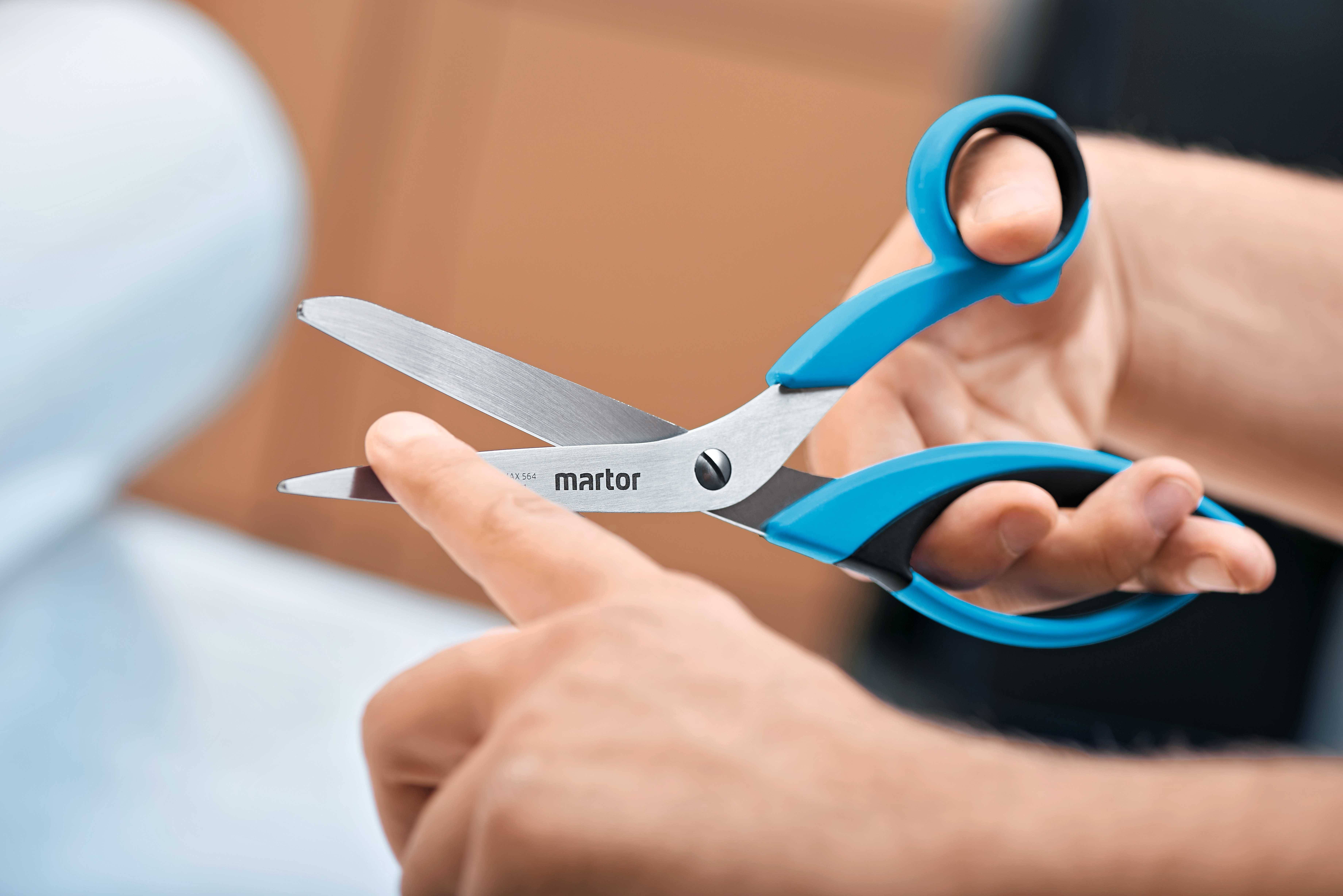 Person hält eine Schere mit blauen Griffen; das Schneiden eines Papiers wird vorbereitet.