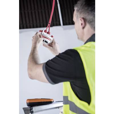 Ein Bauarbeiter in gelber Weste installiert eine Rauchmelder-Deckenmontage. Er steht auf einer Leiter und hält rote Kabel.