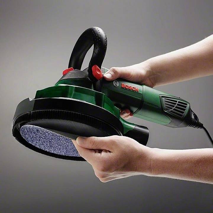 Eine Person hält und verwendet eine grüne Bosch-Poliermaschine. Die Maschine hat einen schwarzen Griff und eine runde Polierscheibe.