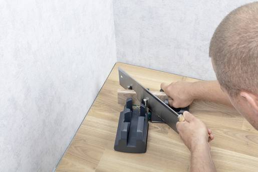 Eine Person schneidet Holz mit einer Gehrungssäge auf einer Holzwerkbank. Fokus liegt auf präzises Zuschneiden für eine Eckverbindung.