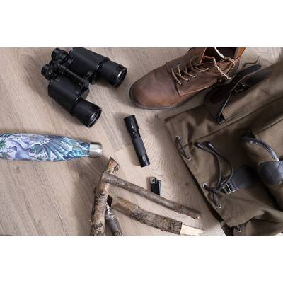 Wanderausrüstung auf Holzboden: Fernglas, Wanderstiefel, Feldflasche, Taschenlampe, Stöcke, Feuerzeug, olivfarbene Tasche.