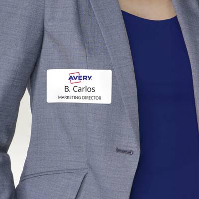 Eine Person trägt ein Namensschild mit der Aufschrift 'B. Carlos, Marketing Director' auf einem grauen Blazer.