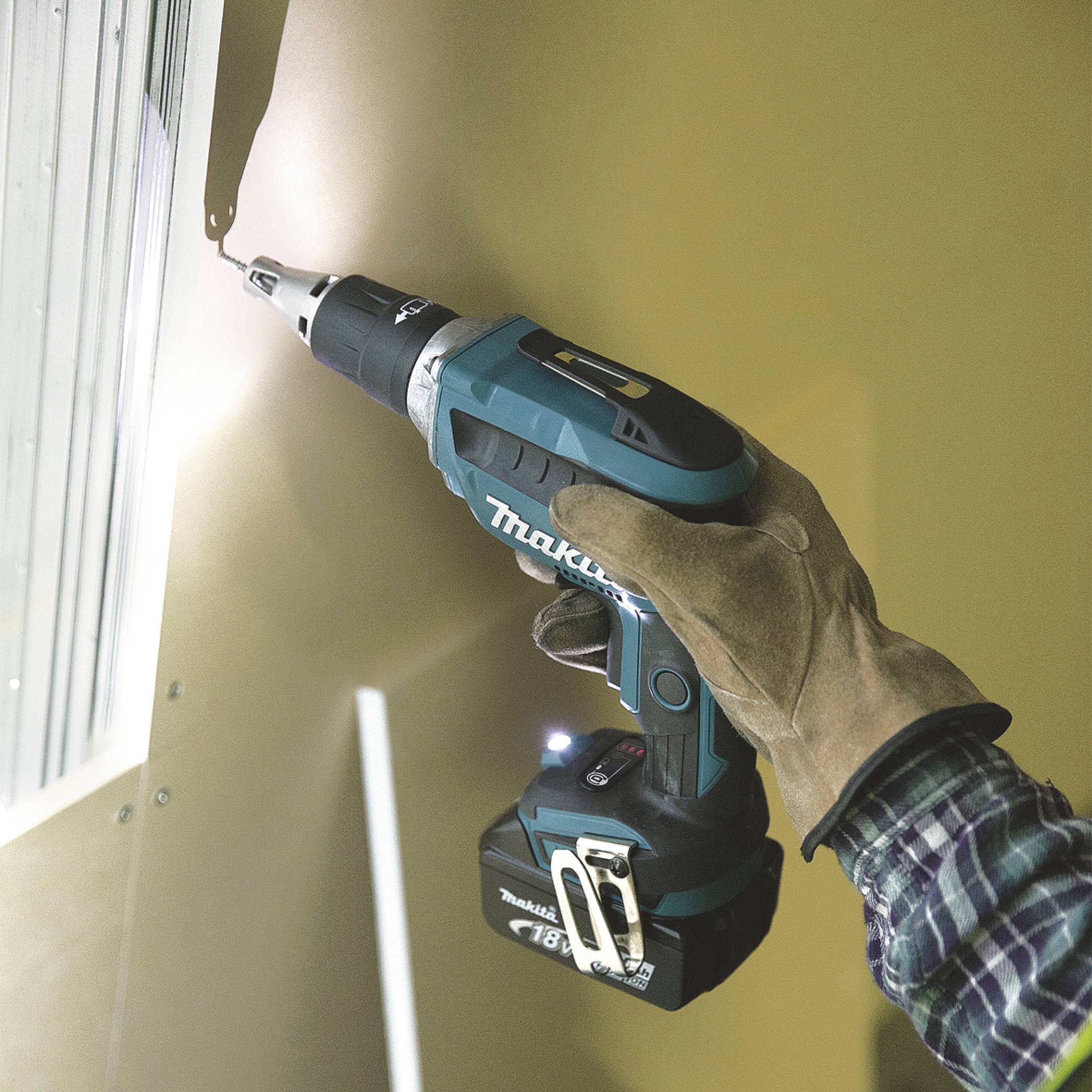 Eine Person bohrt mit einem kabellosen Bohrer in eine Wand. Der Bohrer hat ein blaues Gehäuse, und die Hand trägt einen Arbeitshandschuh.