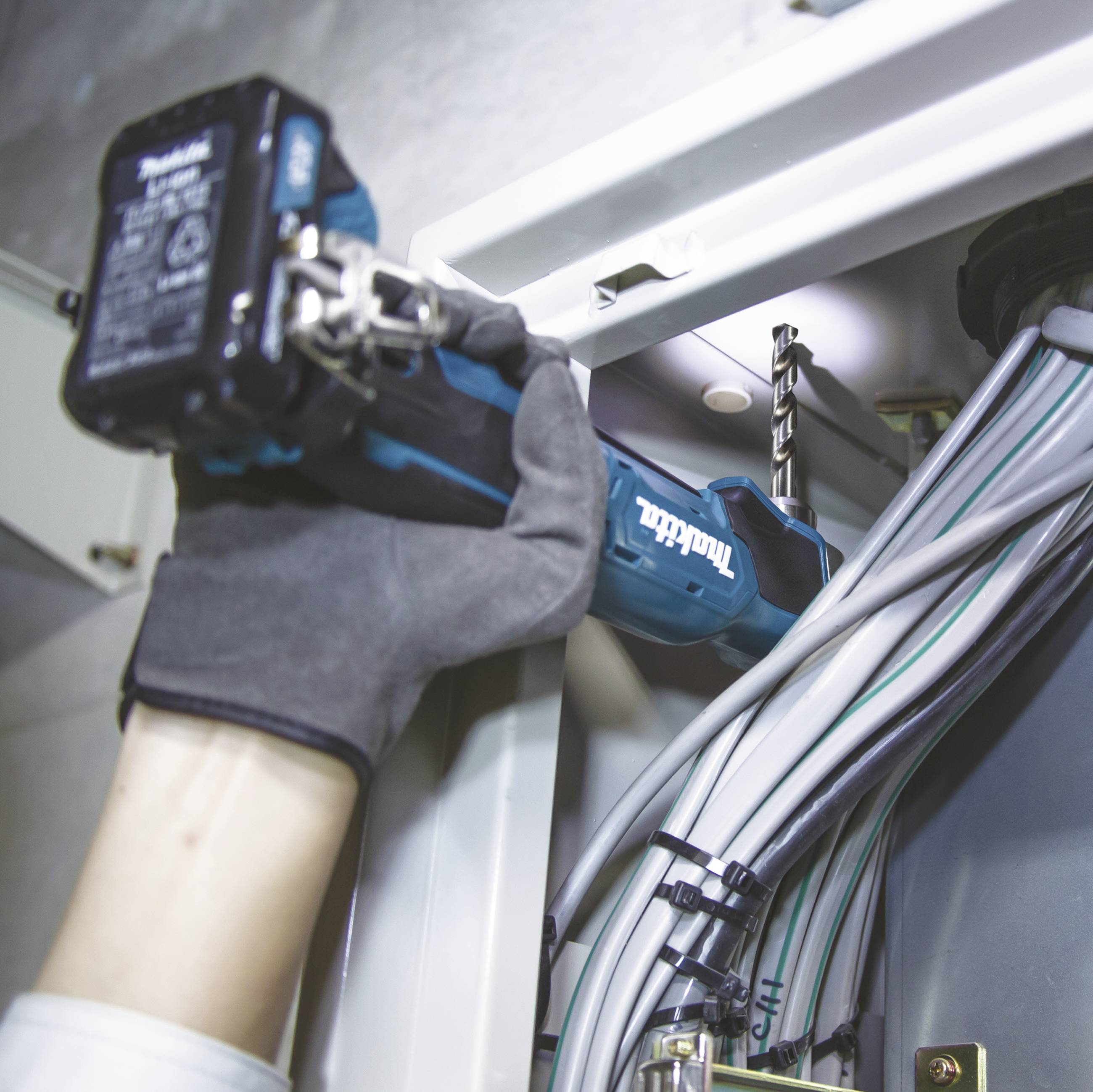 Eine Person befestigt mit einer Bohrmaschine ein Kabelkanalgehäuse an einer Wand. Kabel verlaufen ordentlich durch das Gehäuse.