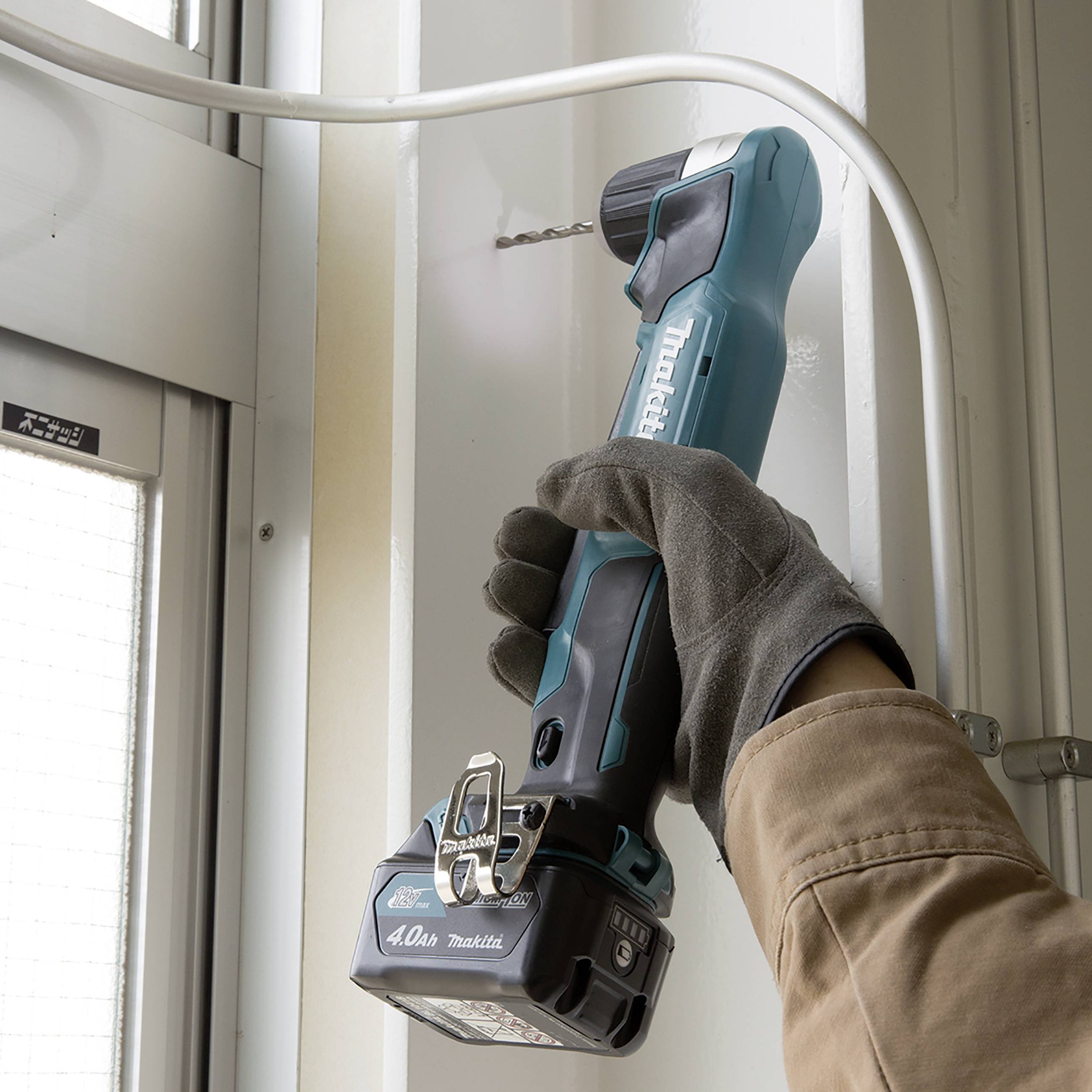 Eine Person bohrt mit einem blauen, kabellosen Akkuschrauber ein Loch in eine weiße Wand, trägt dabei Handschuhe.