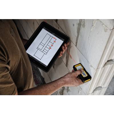 Person hält ein Tablet mit Bauplänen und misst mit einem Laserentfernungsmesser die Wand. Hauptfokus auf Präzisionsmessung.