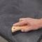 Ein Holzgriff mit der Aufschrift 'SONAX' wird von einer Hand gehalten. Die Bürste wird verwendet, um eine graue Fläche zu reinigen.