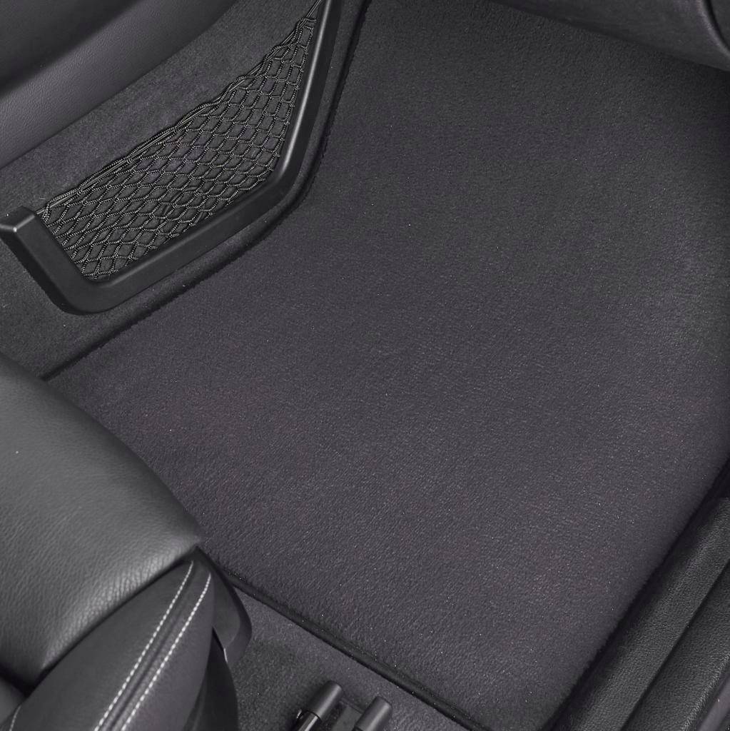Innenraum eines Autos mit schwarzem Bodenbelag und Ledersitz. Der Boden ist sauber und zeigt Pedale im Vordergrund.