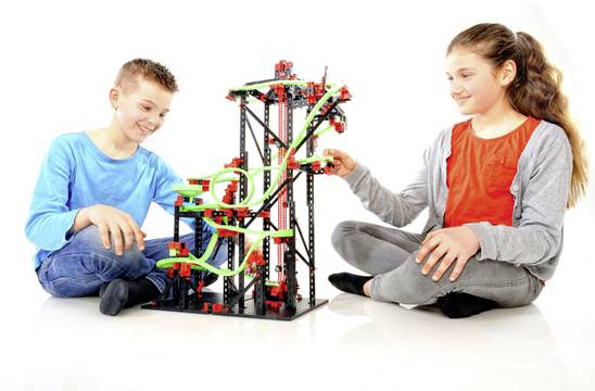 Zwei Kinder spielen mit einer Konstruktionsspielzeugbahn. Sie bauen Teile der Bahn zusammen und scheinen Freude daran zu haben.