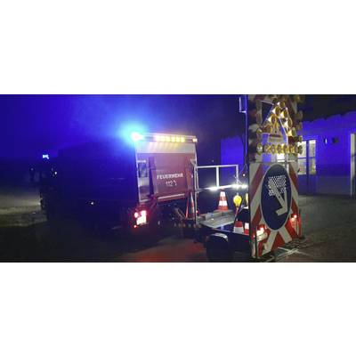 Ein Feuerwehrwagen mit blinkenden blauen Lichtern steht nachts auf einer Straße. Ein Anhänger mit Richtungspfeil weist nach rechts.