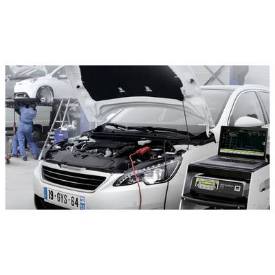 Auto in einer Autowerkstatt mit offener Motorhaube, Batterie wird von einem mit einem Laptop verbundenen Diagnosegerät getestet, während ein Mechaniker im Hintergrund an einem anderen Fahrzeug arbeitet.