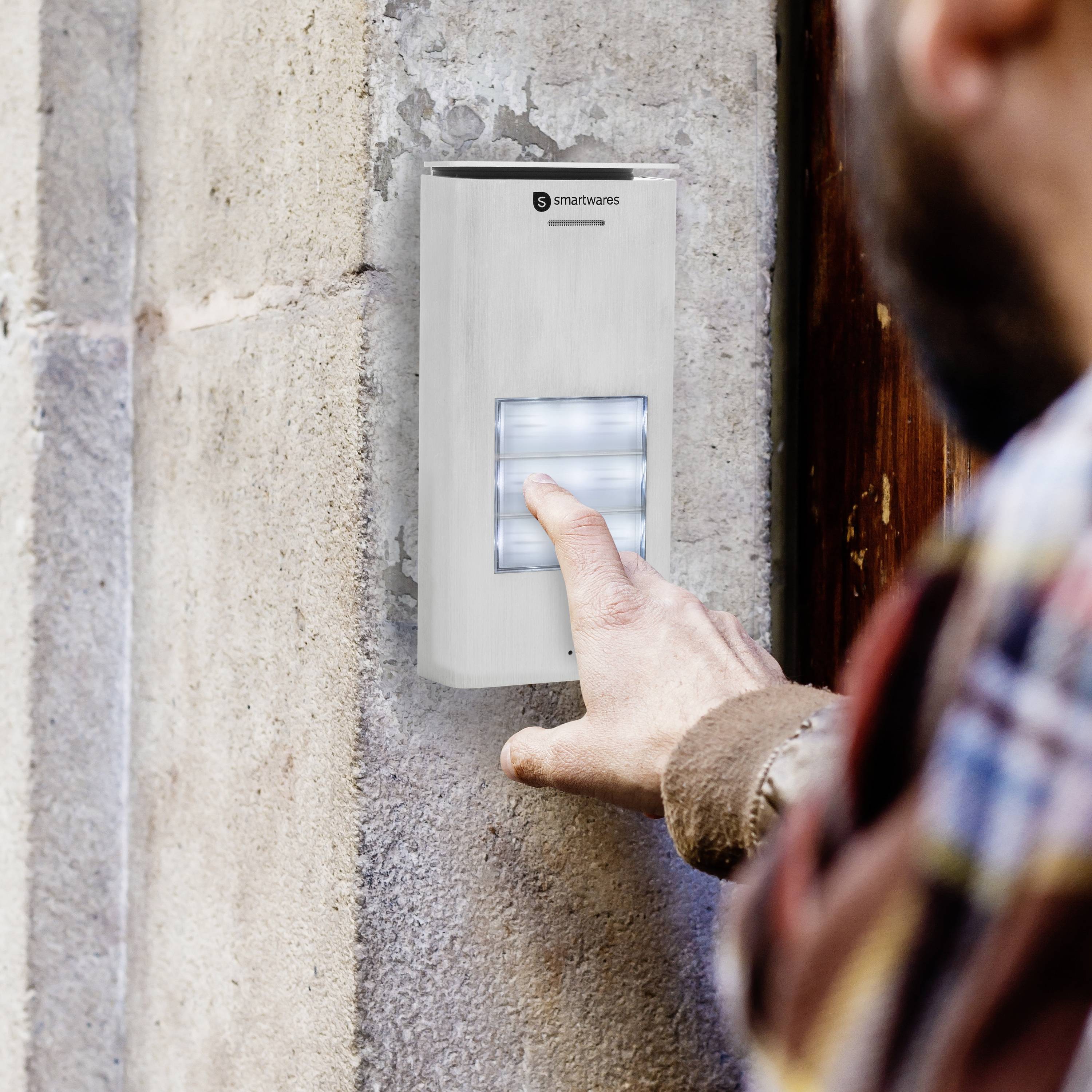 Der Klingelkasten an der Außenwand eines Hauses bietet zusätzliche Beleuchtung der Klingeltaster. Ein Mann ist unscharf im Vordergrund zu sehen. Er ist gerade dabei, zu klingeln.