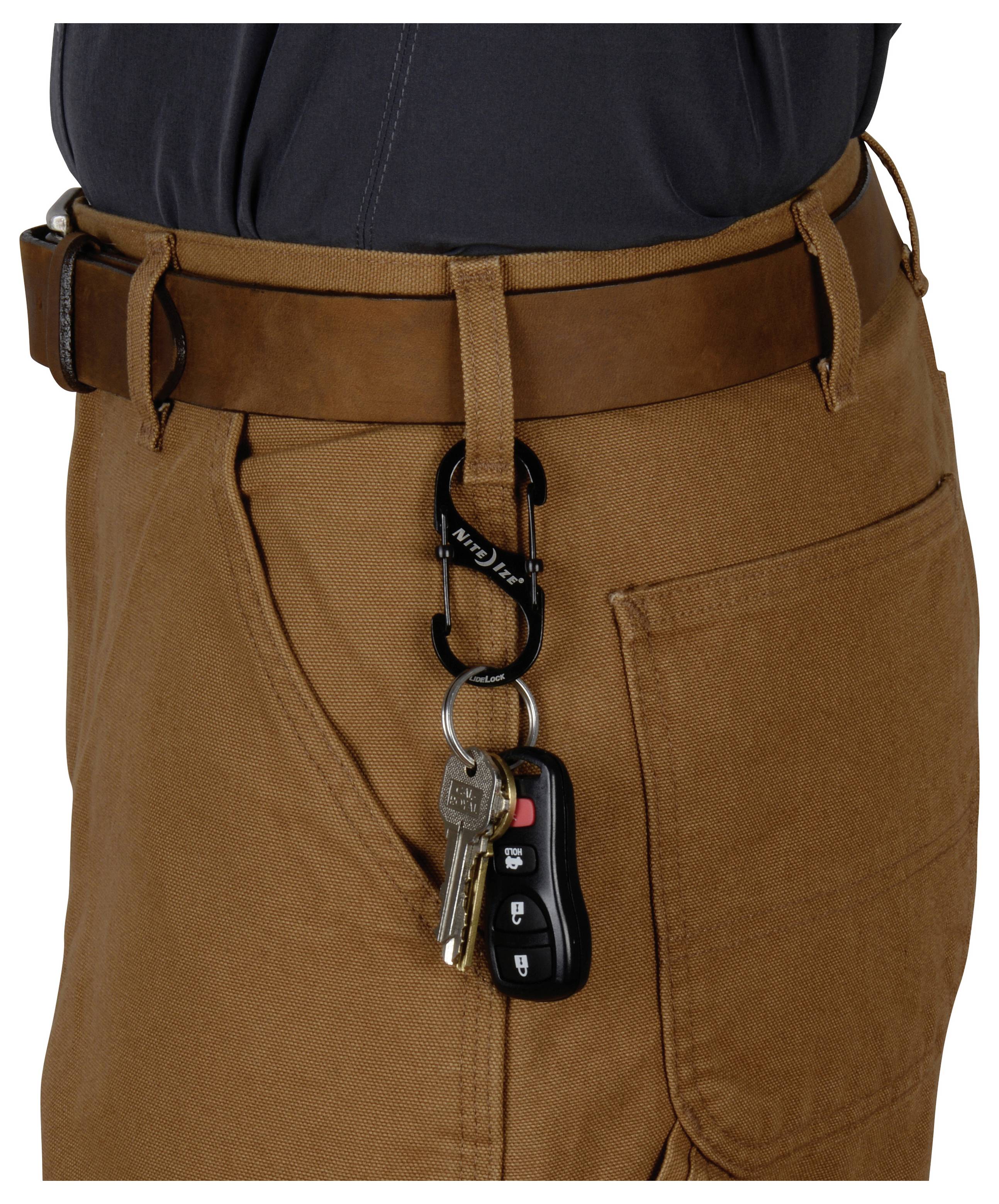 Eine Person, die braune Hosen trägt, mit einem Satz Schlüssel, der an einem Karabiner an der Gürtelschlaufe befestigt ist.