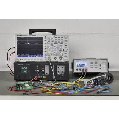 Ein Oszilloskop mit angesteckten Kabeln zeigt eine Kurve. Daneben ein Multimeter und ein Netzteil, die digitale Messwerte anzeigen.