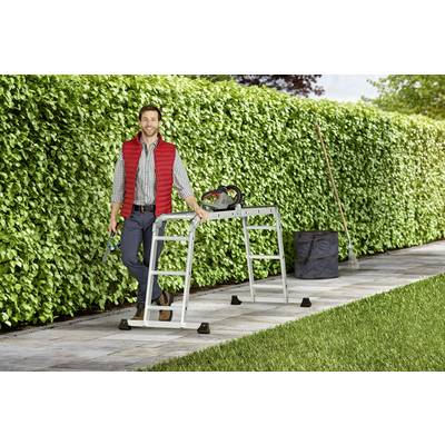 Eine Person lehnt an einer Metallleiter vor einer dichten, grünen Hecke und hält Gartenwerkzeuge. Ein Rechen und eine Tasche sind in der Nähe.
