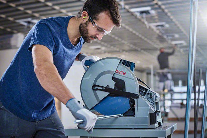 Ein Mann in Schutzbrille und Handschuhen bedient eine elektrische Kreissäge, fokussiert auf seine Arbeit in einer industriellen Umgebung.