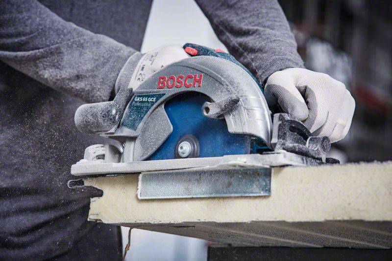 Eine Person schneidet mit einer elektrischen Handkreissäge durch ein Holzbrett. Es gibt viel Staub, der bei der Arbeit entsteht.
