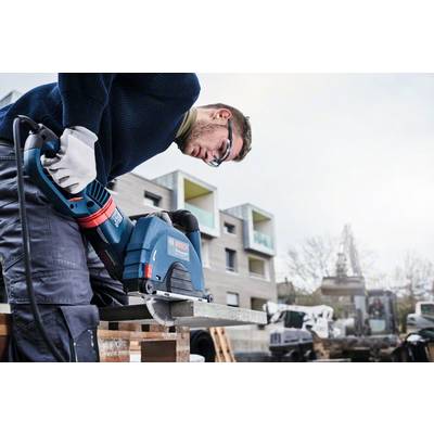 Ein Mann benutzt eine elektrische Säge auf einer Baustelle, um ein Metallstück zu schneiden. Im Hintergrund sind moderne Gebäude sichtbar.