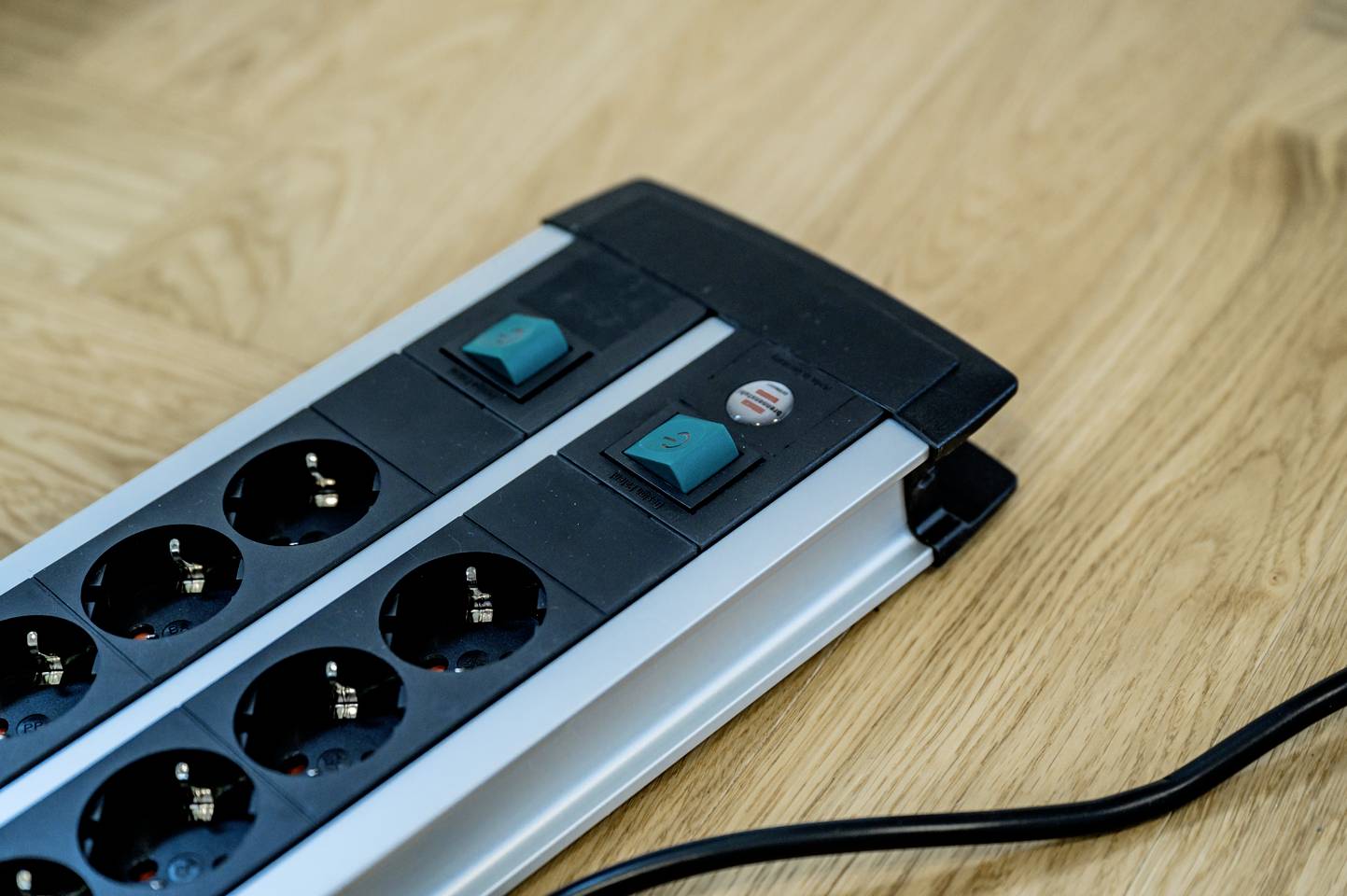 Eine Steckdosenleiste mit acht Steckplätzen und zwei Kippschaltern liegt auf einem Holztisch. Ein Stromkabel ist angeschlossen.
